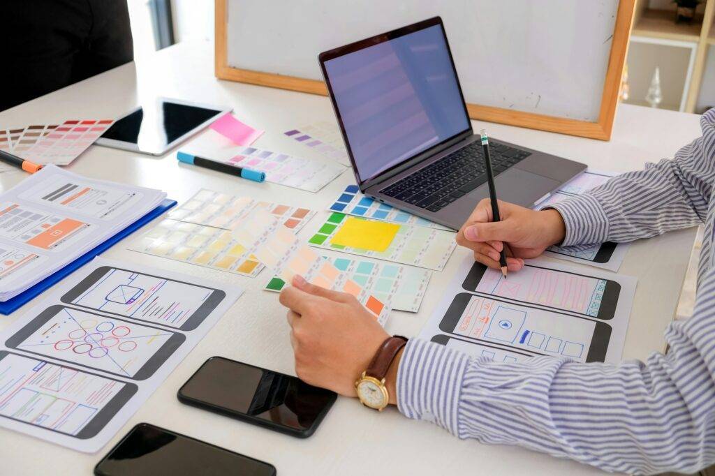 Close-up of man designer hand holding a pencil sketching a web development of a smartphone. laptop p